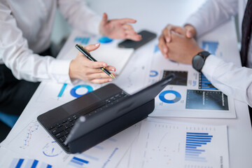 Two people are sitting at a table with a laptop and a pen
