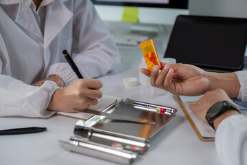 A doctor is writing in a notebook while a patient holds an orange pill bottle