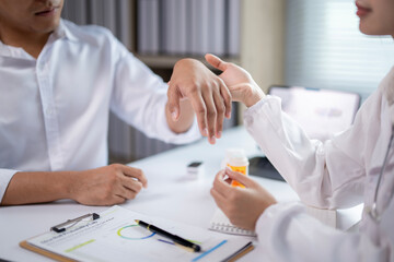 A doctor and a patient are sitting at a desk with a bottle of pills in front of