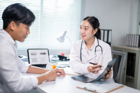 A doctor and a patient are sitting at a desk with a laptop and a tablet