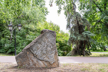 Large granite marble stone monolithic pedestal with cracked yellow brown standing under tree in...