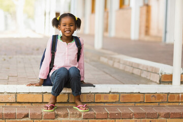 Girl sitting on brick step in school corridor with white columns, wearing pink shirt and backpack