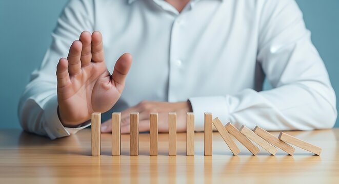Crisp shirted figure halts tumbling blonde wooden dominoes with raised hand a serene tableau against a soft light blue