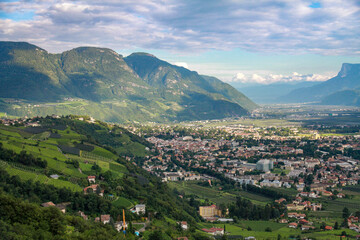 Fototapeta premium Aerial panorama of Adige Valley near Merano: vineyards and orchards under patchy sunlight, Dolomites in blue haze. Perfect for travel and nature themes. South Tyrol, Italy.