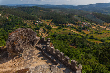 A stone wall with crenellated towers overlooks a picturesque rural landscape