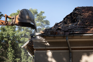 Heavy duty excavator demolishing an old house. Detail on the shingle roof demolish.