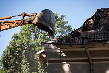 Heavy duty excavator demolishing an old house. Detail on the shingle roof demolish.