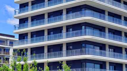 Exterior of a high modern multi-story apartment building - facade, windows and balconies. Modern glass balcony railings.