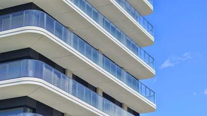Exterior of a high modern multi-story apartment building - facade, windows and balconies. Modern glass balcony railings.