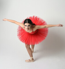 female ballerina dancer model, classical dancing poses stretching with graceful arms. wearing red ballet tutu dress and pointe shoes costume on white isolated studio background.