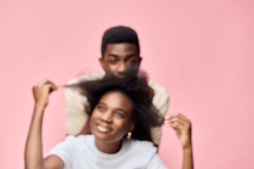 Obraz premium A joyful African couple embracing each other s hairstyles, with a soft pink background, showcasing beautiful natural hair and playful emotions