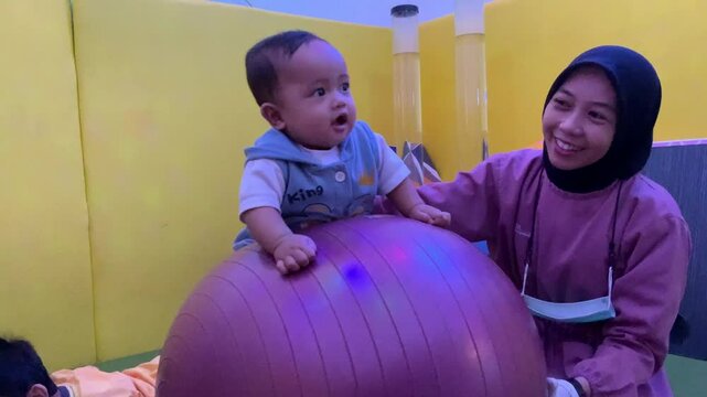 Female physiotherapist assisting baby boy on exercise ball in rehabilitation center