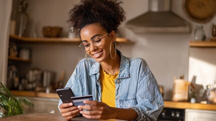 Happy young black African woman customer shopper holding credit card using cell phone mobile app buying fashion clothes paying online making purchase in ecommerce digital store on smartphone at home.