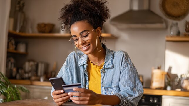 Happy young black African woman customer shopper holding credit card using cell phone mobile app buying fashion clothes paying online making purchase in ecommerce digital store on smartphone at home. - Powered by Adobe