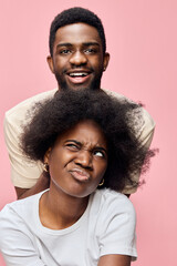 Two young African individuals expressing joy and playful emotion against a pink background,...