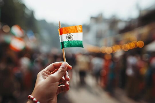 Close-up of a woman's hand holding a small Indian flag, blurry festival background, Independence Day, India, Indian