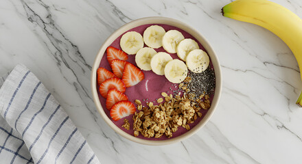 Overhead shot of a smoothie bowl topped with banana slices, strawberries, granola, and chia seeds, with a banana on the side.