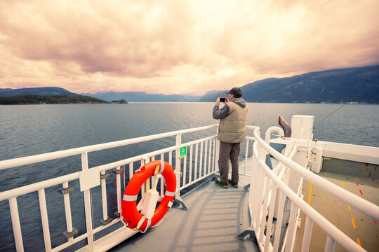A man is sailing on a ferry. A man is standing on the deck and taking a photo from the ship - Powered by Adobe