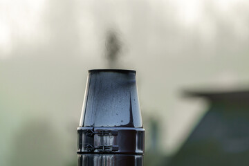 Smoke rises from a chimney in a calm morning landscape surrounded by fog and soft sunlight