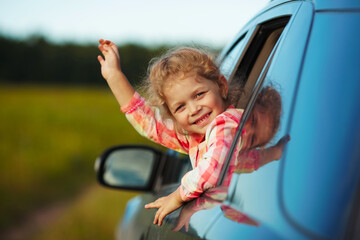 Litle cheerful girl waving from the car.