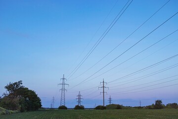 High voltage power transmission towers and power lines on green field at sunset. 