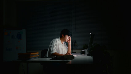 Tired office worker concentrating on his monitor while working alone in a dark office