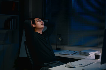 Businessman leaning back in office chair late at night, looking exhausted and stressed