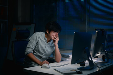 Tired businessman working late at night in a dark office, feeling stressed while looking at computer screen