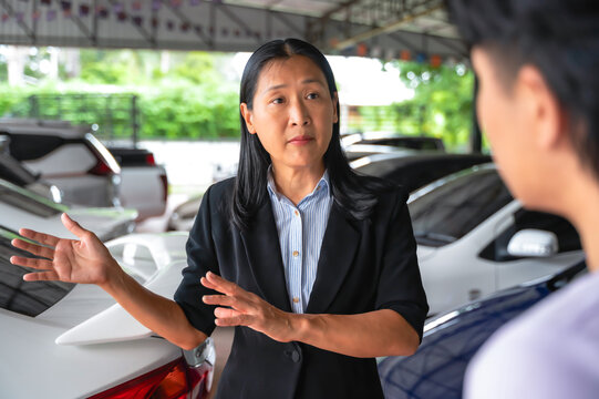 Asian saleswoman presenting car information to male customer in used car dealer shop - Powered by Adobe