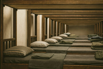Obraz premium Neat row of wooden bunk beds with folded blankets and striped pillows in a simple dormitory, minimal warm interior perfect for shelter, hostel or military barracks atmosphere.
