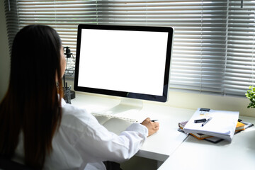 Young entrepreneur working at desk with blank computer screen, taking notes in a notebook
