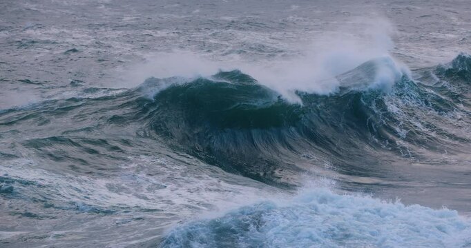 A huge ocean wave curls and breaks on a shallow bombora reef, exploding into a wall of white water during a coastal storm swell. Captured in slow motion.