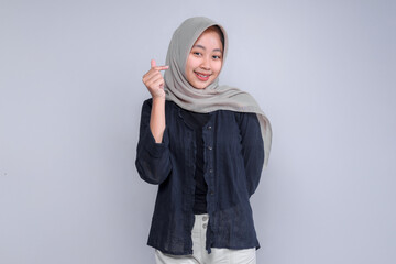 Young Indonesian Muslim woman in a grey hijab and black blouse making a Korean finger heart...