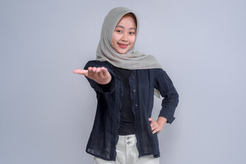 Asian woman wearing a hijab and a black shirt, smiling and extending her hand forward in a...