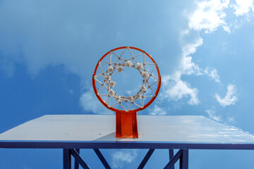 A low-angle shot of a basketball hoop with a clear blue sky in the background. The net is visible,...