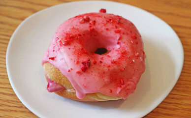 Mouthwatering strawberry glazed with raspberry cream filling doughnut on wooden table