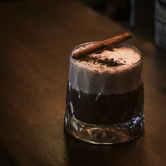 A rich and creamy hot chocolate topped with cinnamon and grated chocolate, served in a textured glass on a wooden table.