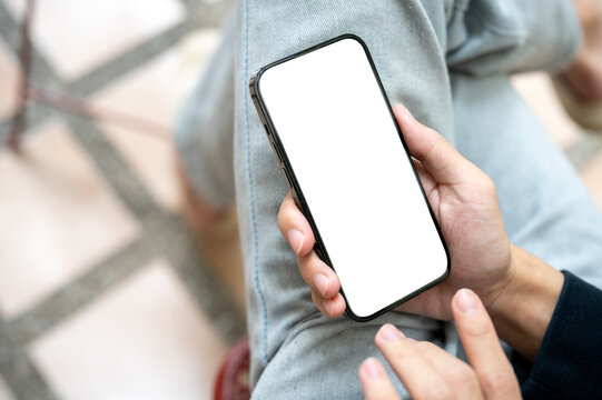 Hand holding white screen smartphone over lap using application or social media while sits on bench.