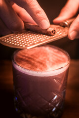 A close-up of a bartender grating a cinnamon stick over a warm cocktail, creating a rich and aromatic finish.