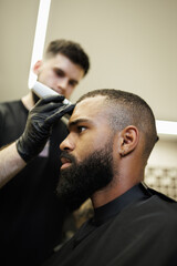 Obraz premium Blurred barber trimming head of bearded african american customer