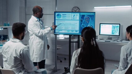 Medium full shot of senior African American male professor in white coat talking about DNA therapy to group of multiethnic university students in research laboratory, demonstrating simulation model - Powered by Adobe