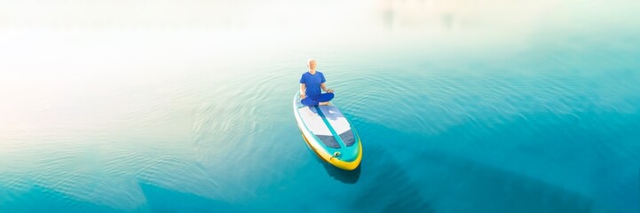 Obraz premium A man doing yoga on his SUP board and practicing mindfulness on his travel.
