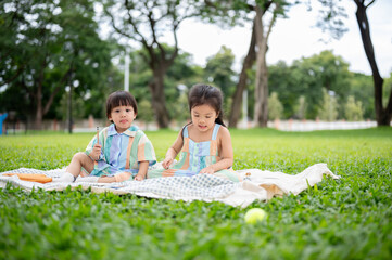 Boy and girl siblings holding pencil drawing while sitting on picnic mat laying over grass in park.