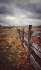 Obraz premium Rustic wooden fence stretches into distant autumn field under dramatic cloudy sky landscape