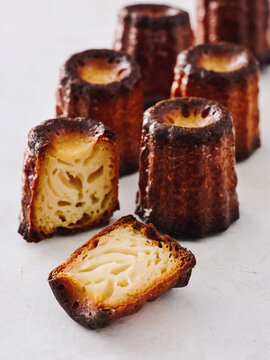 Artisan canele pastries are arranged neatly on a white surface. Their dark, caramelized crust contrasts with the soft, custard-like interior, highlighting unique texture and flavors