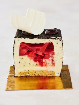 A beautifully designed dessert features layers of creamy filling and a vibrant fruit center. Topped with chocolate and white chocolate decoration, it is served on a gold plate for an elegant touch