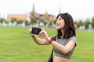 Happy southeast asian woman teenager blogger on solo travel in Bangkok Thailand take photo with...