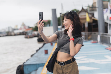 Happy solo southeast asian woman blogger express joy. Local cultural tourism concept experience for world travel explorer with smartphone wait for friend boat Chao Phraya river Bangkok Thailand