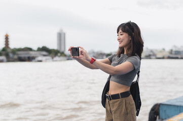 Solo southeast asian woman teenager blogger on boat take photo with smartphone on Chao Phraya River Bangkok. Express world travel explorer asia tourism concept local cultural experience Thailand