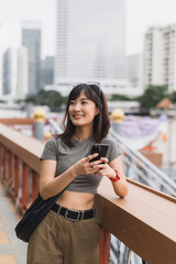 Happy young southeast asian woman teenager blogger using smartphone searching local cultural guide. World travel explorer enjoying asia tourism concept on Chao Phraya river Bangkok experience